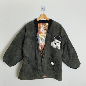 Könnte beinhalten: Eine dunkelgrüne, übergroße Jacke mit schwarzem Kragen und Manschetten. Die Jacke hat ein Porträt von James Dean auf der Vorderseite und ein gemustertes Futter. Die Jacke hat eine lockere Passform und einen Knopfverschluss.