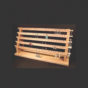 May include: Wooden earring stand with multiple rows of pegs for holding earrings. The stand is made of light wood and has a natural finish. There are several pairs of earrings displayed on the stand, including silver, gold, and turquoise.