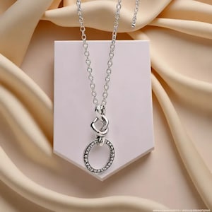 May include: A silver necklace with a pendant featuring a circle with small stones around the edge and a knot design above it.