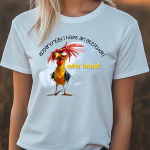Puede incluir: Camiseta blanca con un gallo de dibujos animados con cresta y barbillas rojas. El gallo tiene una expresi&oacute;n de enfado y el texto "&iexcl;aparentemente tengo una actitud! &iexcl;qui&eacute;n lo dir&iacute;a!" est&aacute; impreso en la camiseta.