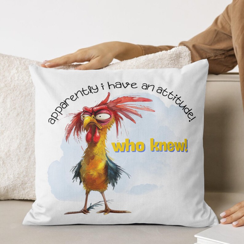 Puede incluir: Almohada blanca con un gallo de dibujos animados con cresta roja y plumas amarillas. El gallo tiene una expresi&oacute;n gru&ntilde;ona y el texto "&iexcl;aparentemente tengo una actitud! &iexcl;qui&eacute;n lo sab&iacute;a!" est&aacute; impreso en la almohada.