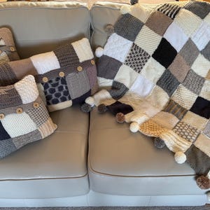 Pu&ograve; includere: Un set di cuscini e una coperta in stile patchwork nei toni neutri del grigio, crema e nero. I cuscini hanno dettagli con bottoni. La coperta, con bordi a pompon, &egrave; appoggiata su un divano chiaro.