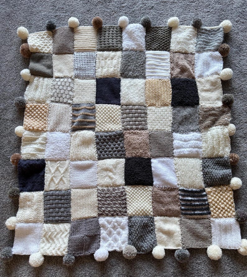 Pu&ograve; includere: Una coperta patchwork lavorata a maglia in varie tonalit&agrave; di bianco, crema, grigio e marrone. La coperta &egrave; composta da quadrati con diverse trame e motivi ed &egrave; rifinita con piccoli pompon.