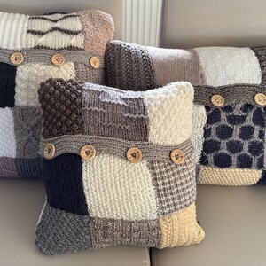 Pu&ograve; includere: Quattro cuscini decorativi con un design patchwork. Ogni cuscino presenta una variet&agrave; di trame e colori a maglia, tra cui bianco, grigio, nero e beige. Bottoni in legno adornano una fascia al centro di ogni cuscino, aggiungendo un tocco rustico.