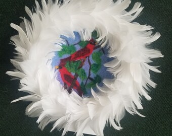 Corona de plumas blancas de 10 pulgadas con cardenales de fieltro tapiz en el centro.
