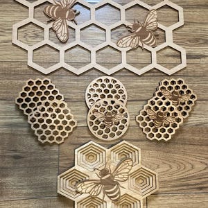 May include: A collection of wooden bee-themed decorations. The set includes honeycomb-shaped wall art, coasters, and decorative pieces, all featuring bee cutouts. The items are made of light-coloured wood and are displayed on a wooden surface.