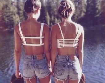 May include: Two people stand facing away from the camera, wearing white crop tops and denim shorts. The crop tops have unique strap designs. The background features a lake and trees. The Instagram handle "firegypsyvintage" is visible at the top.