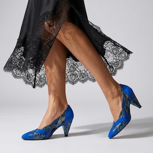 May include: A black skirt with a scalloped lace hem and a pair of vibrant blue high-heeled shoes. The shoes feature a pointed toe, a mid-height heel, and a crisscross strap design with a textured, multi-colored snakeskin-like pattern on the sides.