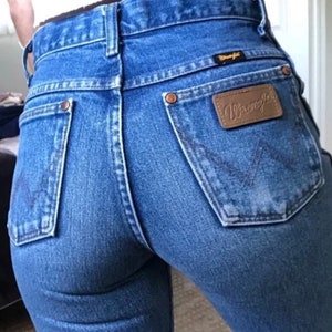 Op de afbeelding: Een paar blauwe denim jeans met een bruine leren Wrangler-patch op de achterzak.