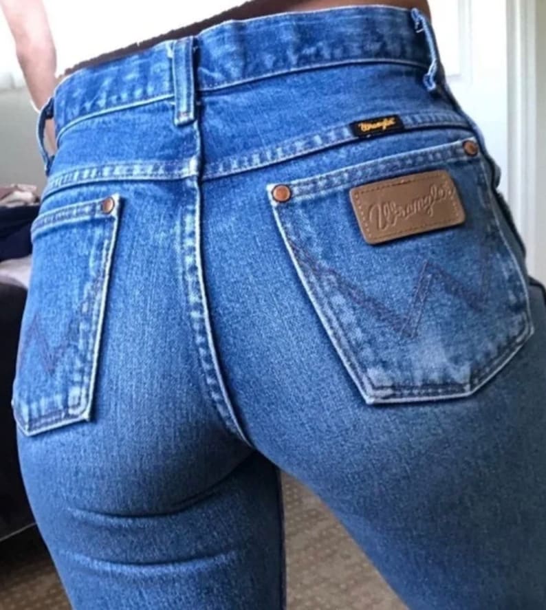 Op de afbeelding: Een paar blauwe denim jeans met een bruine leren Wrangler-patch op de achterzak.