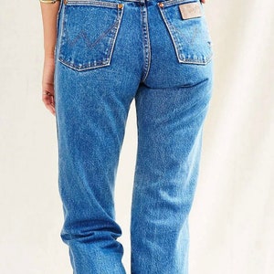 Op de afbeelding: Een paar blauwe denim jeans met een hoge taille en een rechte pijp. De jeans heeft een lichte wassing en een verbleekte look. De achterzakken hebben een gestikt ontwerp en een lederen patch met de merknaam "Wrangler" erop.