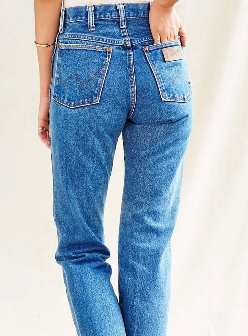 Op de afbeelding: Een paar blauwe denim jeans met een hoge taille en een rechte pijp. De jeans heeft een lichte wassing en een verbleekte look. De achterzakken hebben een gestikt ontwerp en een lederen patch met de merknaam "Wrangler" erop.