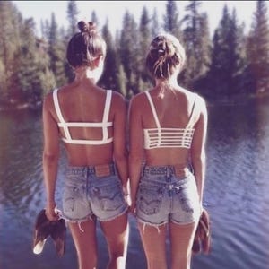 May include: Two white bralettes with distinct strap designs worn with light blue denim shorts. One bralette features a wide horizontal strap back, while the other has a multi-strap cage back. Both garments are shown from the back view.