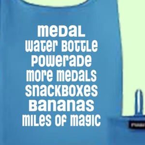 May include: A light blue reusable shopping bag, with the words "medal, water bottle, Powerade, more medals, snackboxes, bananas, miles of magic" printed in white. The bag is shown both open and folded. The folded bag has a small handle.