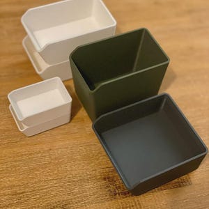 May include: Four plastic storage containers, two white and two green. The white containers are stacked on top of each other. The green containers are separate.
