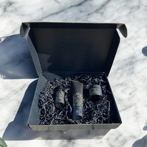 Beauty Wavez skincare gift set with cleanser, vitamin C serum, and facial shea butter in a premium black box with gold accents, styled on a luxury white marble background with eucalyptus sprigs.