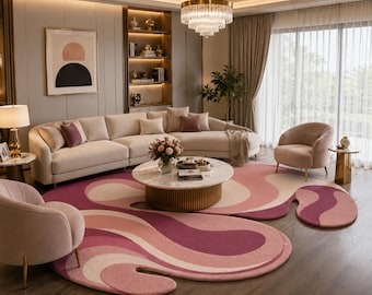 May include: A large, irregularly shaped area rug featuring a wavy, abstract pattern in shades of pink, magenta, and cream. The rug is positioned on a dark wood floor in a living room, centered beneath a round marble coffee table with a gold base.