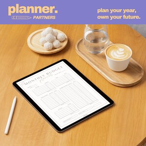 以下が含まれることがあります： 「月間予算プランナー」のレイアウトを表示するデジタルタブレットと白いスタイラス。 木製のトレイには水とコーヒーカップが入っており、小さなプレートには白いココナッツボールが載っています。 テキスト「plan your year, own your future」が表示されています。
