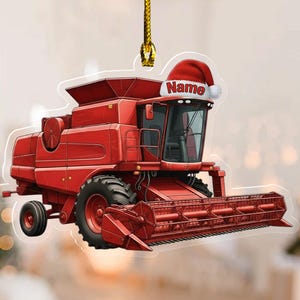 May include: A red combine harvester ornament with a Santa hat and the word "Name" on the cab. The ornament is hanging from a gold string. The combine has large black tires and a detailed design.