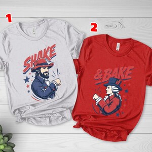May include: A light gray t-shirt labeled 1 featuring a graphic of a man in a red hat with the text SHAKE and a red t-shirt labeled 2 featuring a graphic of a man in a blue hat with the text & BAKE, both with blue and red star accents.