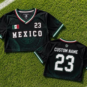 May include: A black cropped jersey with a V-neck featuring green, white, and red trim. The front displays the text MEXICO, the number 23, and a small Mexican flag. The back shows the text CUSTOM NAME and the number 23 in white lettering.