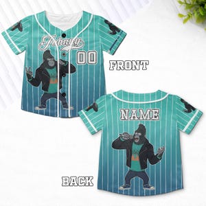 May include: A teal and white baseball jersey featuring a cartoon gorilla with a microphone. The front of the jersey has the name "Johnny" and the number "00". The back of the jersey has the word "NAME".