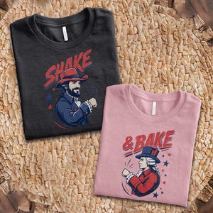 May include: A black t-shirt featuring a graphic of a man in a colonial hat with the text SHAKE and a pink t-shirt featuring a graphic of a person in a colonial hat with the text & BAKE, both decorated with blue and red stars and accents.