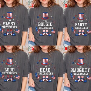 May include: A charcoal gray t-shirt featuring a graphic with a red, white, and blue top hat, fireworks, a small American flag, and shoes. The text reads THE SASSY, BOUGIE, PARTY, LOUD, HEAD, or NAUGHTY FIRECRACKER, depending on the specific numbered option.