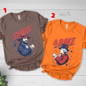May include: A brown t-shirt with the text SHAKE and a graphic of a person in a red hat and blue coat, and an orange t-shirt with the text & BAKE and a graphic of a person in a blue hat and red coat, both featuring star accents.