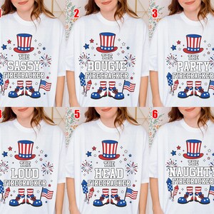 May include: A white t-shirt featuring a patriotic graphic with a red, white, and blue top hat, fireworks, a rocket, an American flag, and blue shoes. The text reads THE SASSY, BOUJIE, PARTY, LOUD, HEAD, or NAUGHTY FIRECRACKER, numbered one through six.