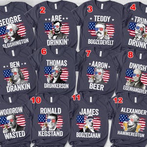 May include: A collection of navy blue t-shirts featuring portraits of historical figures wearing sunglasses and holding beer mugs. Each shirt has a unique pun-based name, such as "GEOGRE SLOSHINGTON" and "TRUMP DRUNK", with an American flag design.