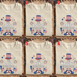 May include: A beige t-shirt featuring a graphic of a red, white, and blue top hat, fireworks, a rocket, and shoes. The text reads THE SASSY, BOUGIE, PARTY, LOUD, HEAD, or NAUGHTY FIRECRACKER. The design includes a small American flag illustration.