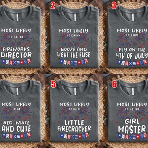 Puede incluir: Una colecci&oacute;n de seis camisetas gris oscuro, cada una con texto blanco y gr&aacute;ficos de fuegos artificiales y banderines en rojo, blanco y azul. Las camisetas muestran frases como Most Likely to be the Fireworks Director y otras variantes.