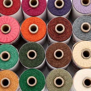 Könnte beinhalten: Eine Sammlung von 20 Spulen gewachsten Leinenfadens in verschiedenen Farben, darunter Rot, Orange, Gelb, Grün, Blau, Lila, Braun und Weiß. Die Spulen sind in einem Rastermuster auf weißem Hintergrund angeordnet.