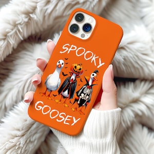 May include: Orange phone case with the words "SPOOKY GOOSEY" in white script. The case features three cartoon geese dressed in Halloween costumes: a vampire, a jack-o'-lantern, and a skeleton. Small black bats are also included in the design.