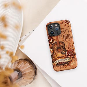 May include: A phone case with a brown background featuring a detailed illustration of an acoustic guitar, roses, and the text "Just a Girl Who Loves Country Music." The case has a glossy finish and a camera cutout.