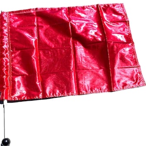 May include: A bright red flag with a shiny, metallic finish. The flag is attached to a white pole with a black ball at the end.
