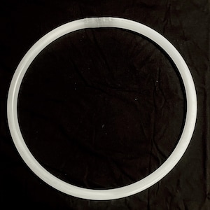 May include: A white, circular object, possibly a necklace or decorative item, against a black background. The object is a complete circle with a slight gap at the top. The material appears to be smooth and opaque.