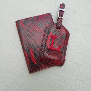 May include: Red and black snakeskin passport holder and luggage tag with the letter L embroidered in red.