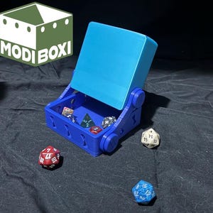 May include: A blue and teal dice rolling box with a hinged lid. The box is open and there are several dice inside. The box is made of plastic and has a smooth finish.