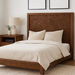 Puede incluir: Una cama de madera con cabecero tallado, con edredón y almohadas color crema. Se ve una mesita de noche a juego con una lámpara y una planta. La habitación tiene una paleta de colores neutros.