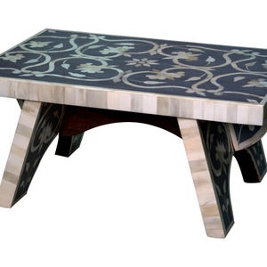 May include: A small, rectangular wooden table with a dark surface inlaid with a floral pattern. The legs and edges are light-colored, creating a contrast. The table is approximately 18 inches long, 12 inches wide, and 10 inches tall.