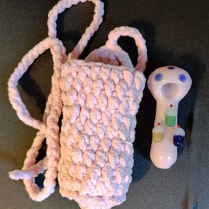 May include: A pink crocheted pouch with a long strap and a pink glass pipe with blue accents and three cupcake designs.