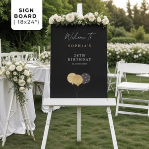 May include: A black sign board (18x24 inches) with white text that reads "Welcome to Sophia's 28th Birthday 26.June.20XX". The sign has gold and black balloon graphics and is decorated with white flowers.