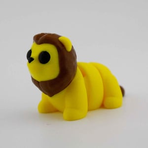 Op de afbeelding: Een gele leeuwenfiguur met een bruine manen en staart. De leeuw heeft zwarte ogen en kruipt. Het figuur is gemaakt van een zacht materiaal, waarschijnlijk een speelgoed of decoratieartikel.