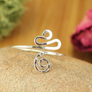 May include: A silver ring with a hammered finish and a unique, abstract design. The ring is made of a single piece of wire that is twisted and shaped into a spiral and a flowing, organic form.