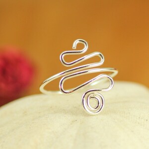 May include: A silver ring with a unique, abstract design. The ring is made of wire that is twisted and shaped into a series of loops and curves.