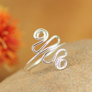 May include: A silver wire ring with a unique, abstract design. The ring is made of thin wire that is twisted and shaped into a series of loops and curves.