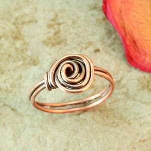 May include: A copper wire ring with a double spiral design. The ring is made of two different shades of copper wire.