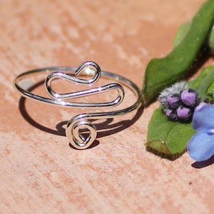 May include: A silver ring with a unique, abstract design. The ring is made of thin wire that is twisted and shaped into a flowing, organic pattern.